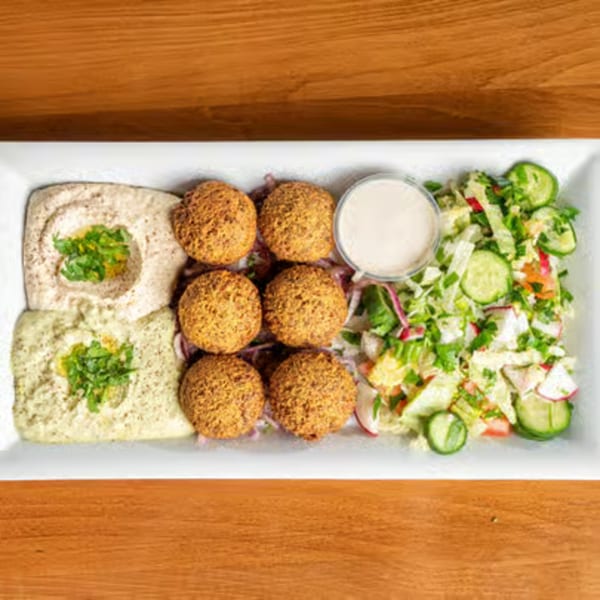A white rectangular plate with falafel, two types of hummus, and a fresh salad.