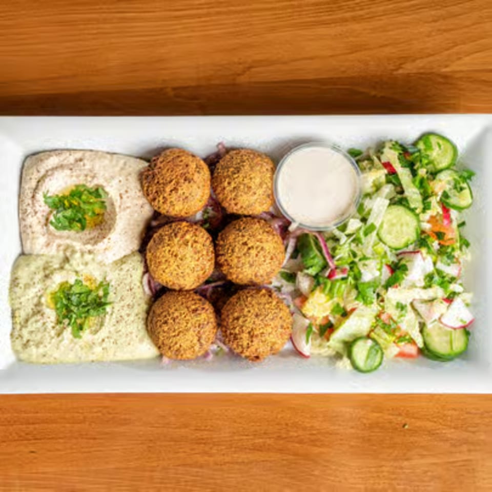 A white rectangular plate with falafel, two types of hummus, and a fresh salad.