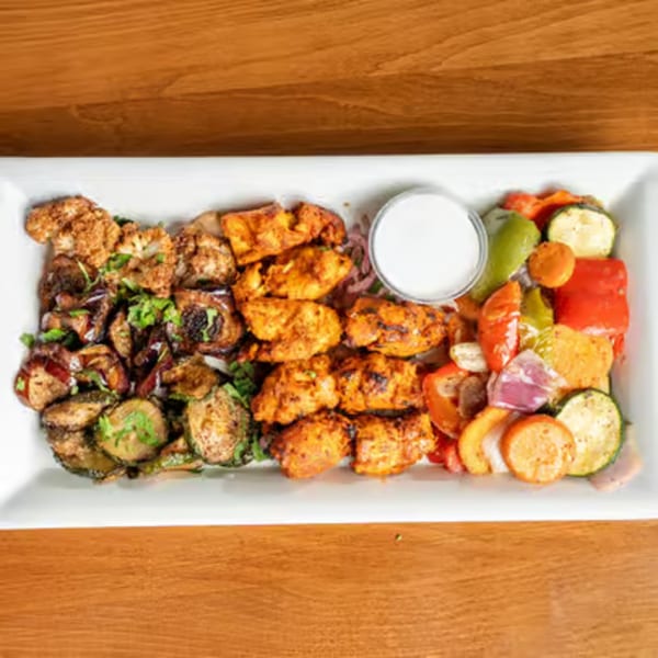 A white platter with grilled chicken, roasted vegetables, and a side of white sauce.
