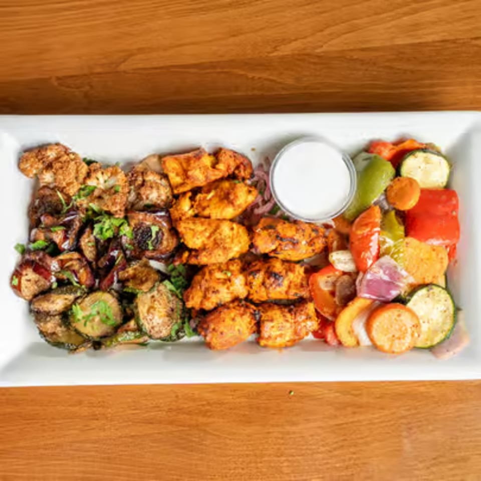 A white platter with grilled chicken, roasted vegetables, and a side of white sauce.