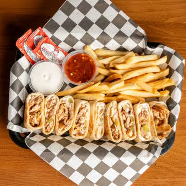 A basket of chicken shawarma wraps, fries, ketchup packets, garlic sauce, and chili sauce.
