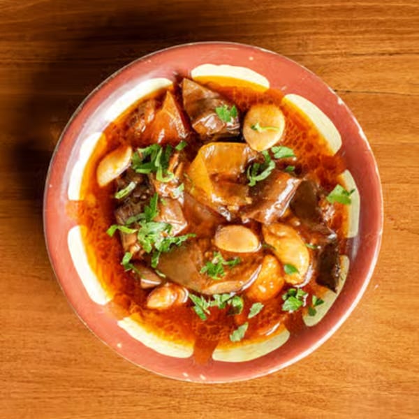 Overhead view of a red bowl filled with a rich stew, garnished with fresh parsley.