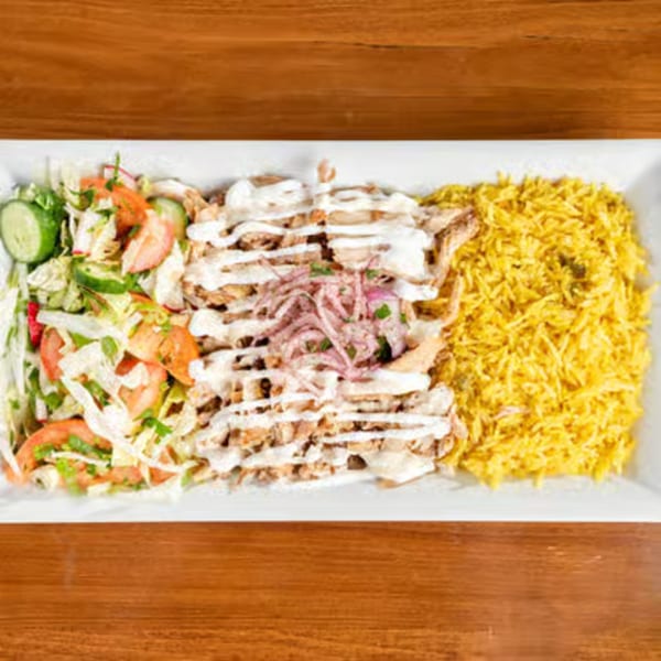 A white rectangular plate with chicken shawarma, yellow rice, and a fresh salad.