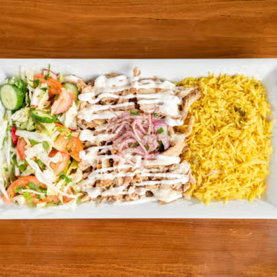 A white rectangular plate with chicken shawarma, yellow rice, and a fresh salad.