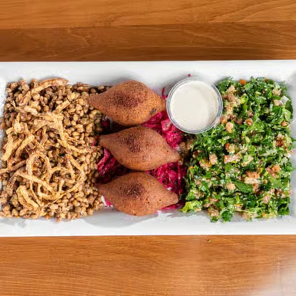 A white rectangular platter with kibbeh, bulgur, fried onions, pickled cabbage, salad, and a dip.