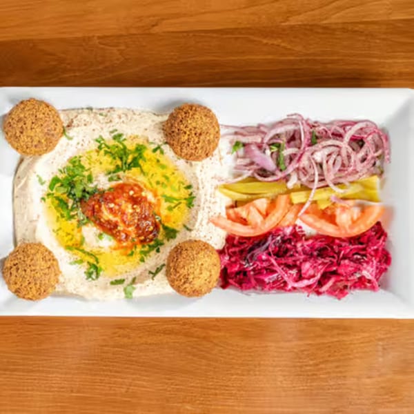 A white rectangular plate with hummus, falafel, red cabbage, sliced tomatoes, and pickled vegetables.