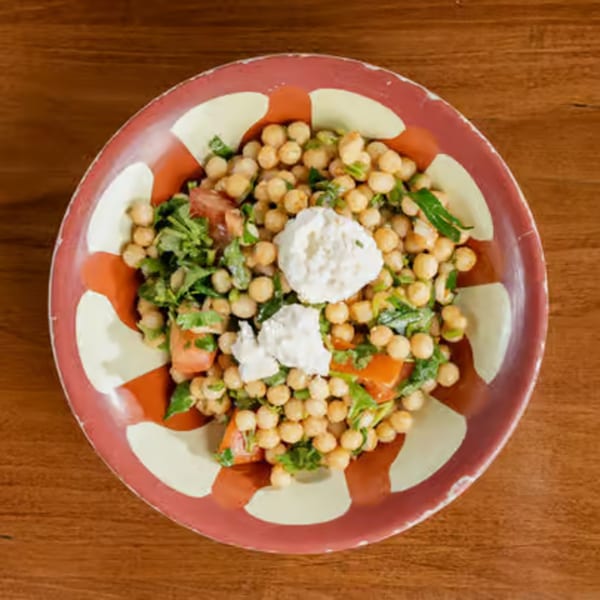 Chickpea salad with tomatoes, greens, and feta cheese in a decorative red and white bowl.